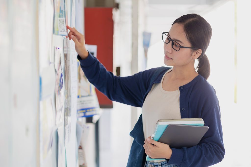 University school teen girl looking for job part time work post at campus advertising billboard.